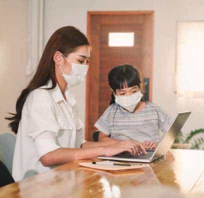 A mother wearing a mask, looking at Covid 19 resources while her young daughter observes.