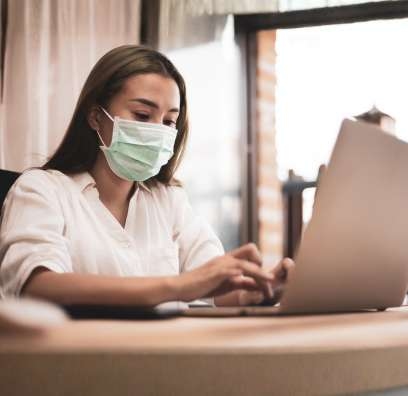 A young woman wearing a mask and looking at a laptop, looking at Covid 19 resources.